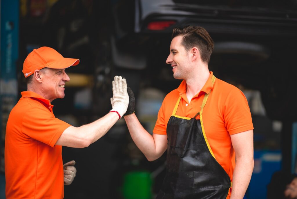 a portrait group photo of machanic team smiling in front of garage with thumb up